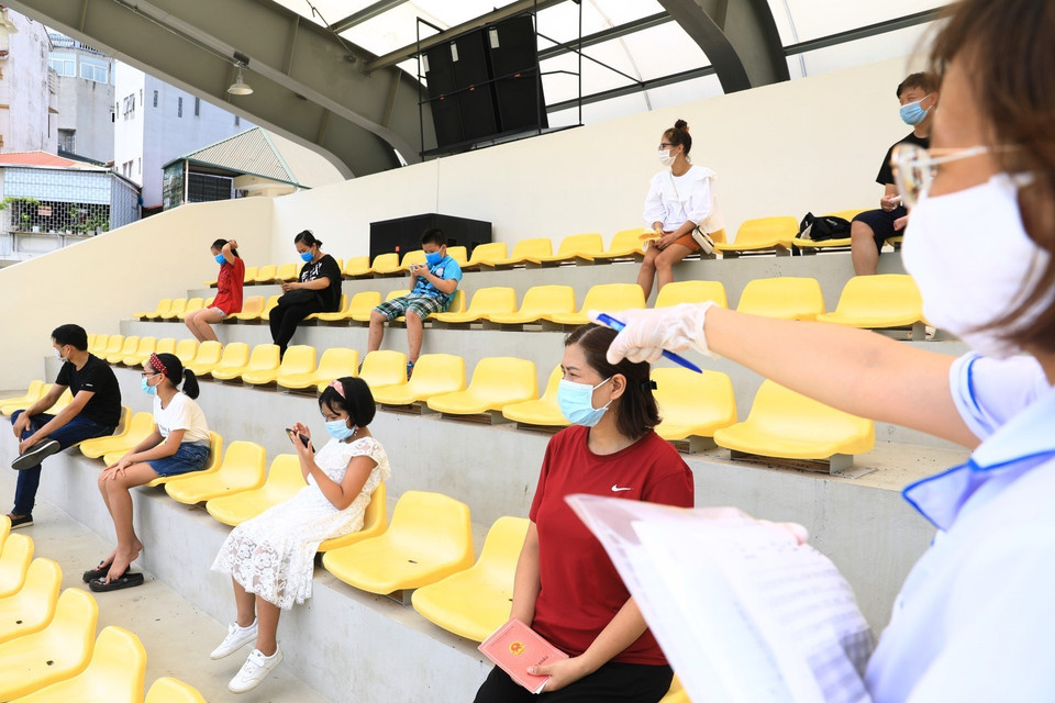 Nhân viên y tế quận Đống Đa hướng dẫn người dân ngồi giãn cách đúng quy định trước khi lấy mẫu xét nghiệm RT-PCR.(Ảnh: Thành Đạt/TTXVN)