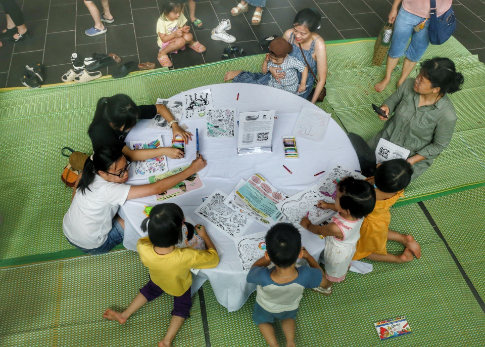 Em nhỏ cùng phụ huynh tô màu tranh dân gian. (Ảnh: Tuấn Đức/TTXVN)