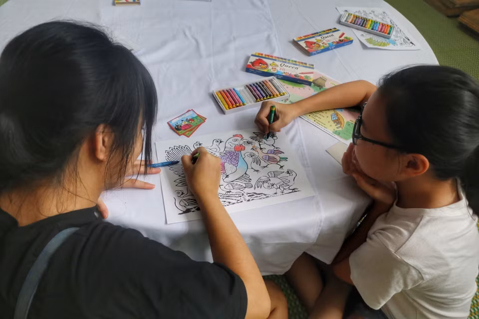 Em nhỏ cùng phụ huynh tô màu tranh dân gian. (Ảnh: Tuấn Đức/TTXVN)