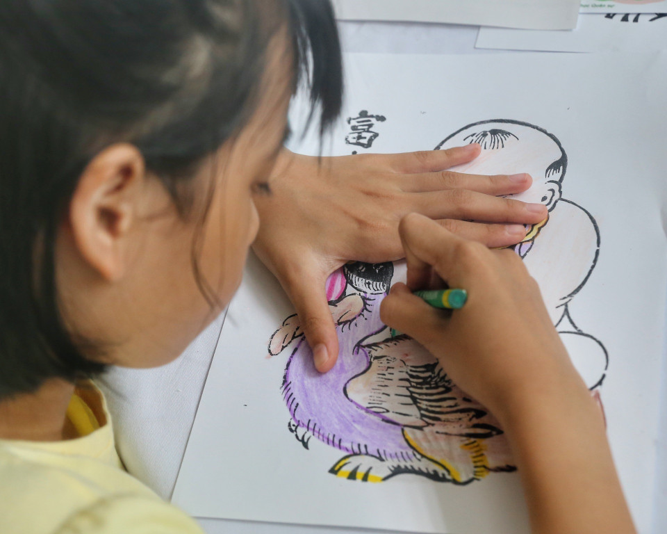 Em nhỏ trải nghiệm tô màu tranh dân gian. (Ảnh: Tuấn Đức/TTXVN)