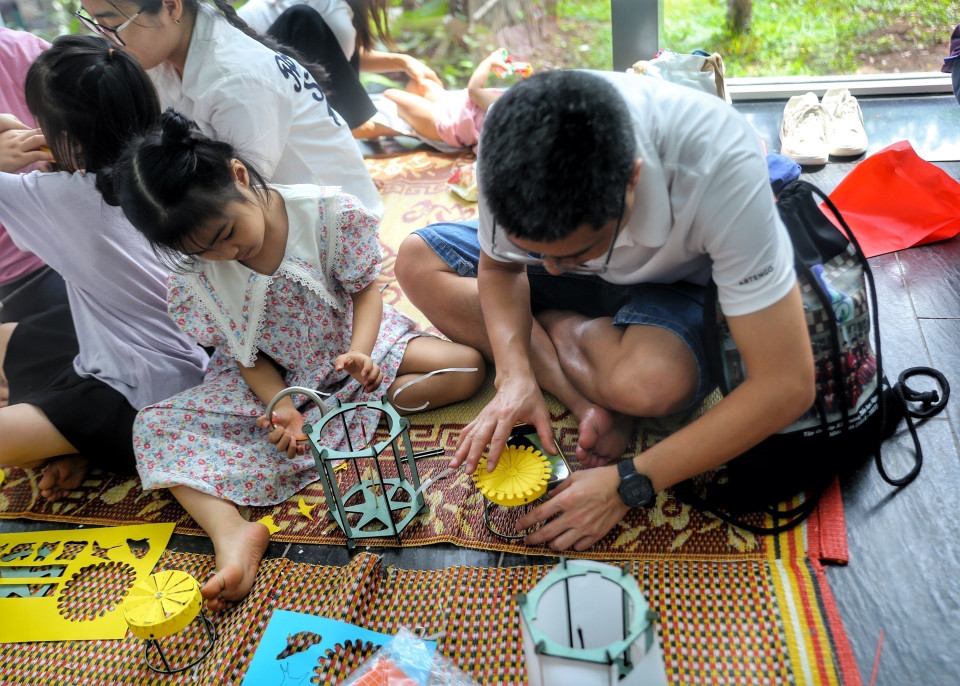Em nhỏ cùng phụ huynh trải nghiệm làm đèn lồng. (Ảnh: Tuấn Đức/TTXVN)