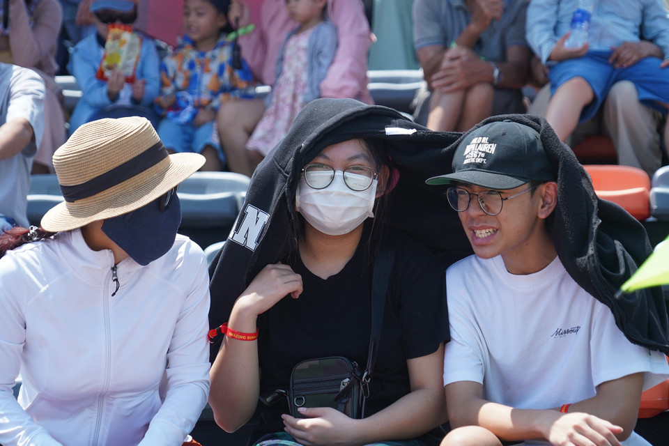 Đôi bạn trẻ chia nhau chiếc áo khoác để che nắng. (Ảnh: Việt Anh/Vietnam+)