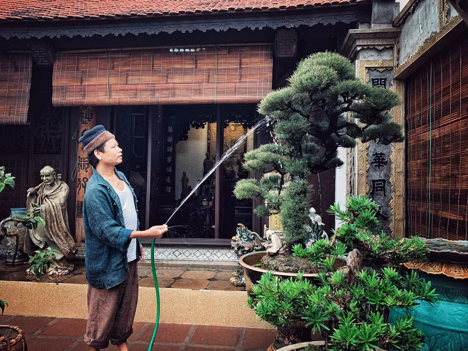 Một buổi sớm ngày cận Tết, vận chiếc quần đũi sắn ống thấp ống cao với đôi tông lào ngả màu, nghệ nhân ưu tú Trần Nam Tước say sưa tưới tắm cho vườn tiểu cảnh trên sân thượng. (Ảnh: Xuân Mai/Vietnam+)