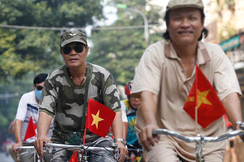 Thành viên các câu lạc bộ đạp xe diễu hành với cờ Tổ quốc phía trước. (Ảnh: Hoàng Việt/TTXVN)