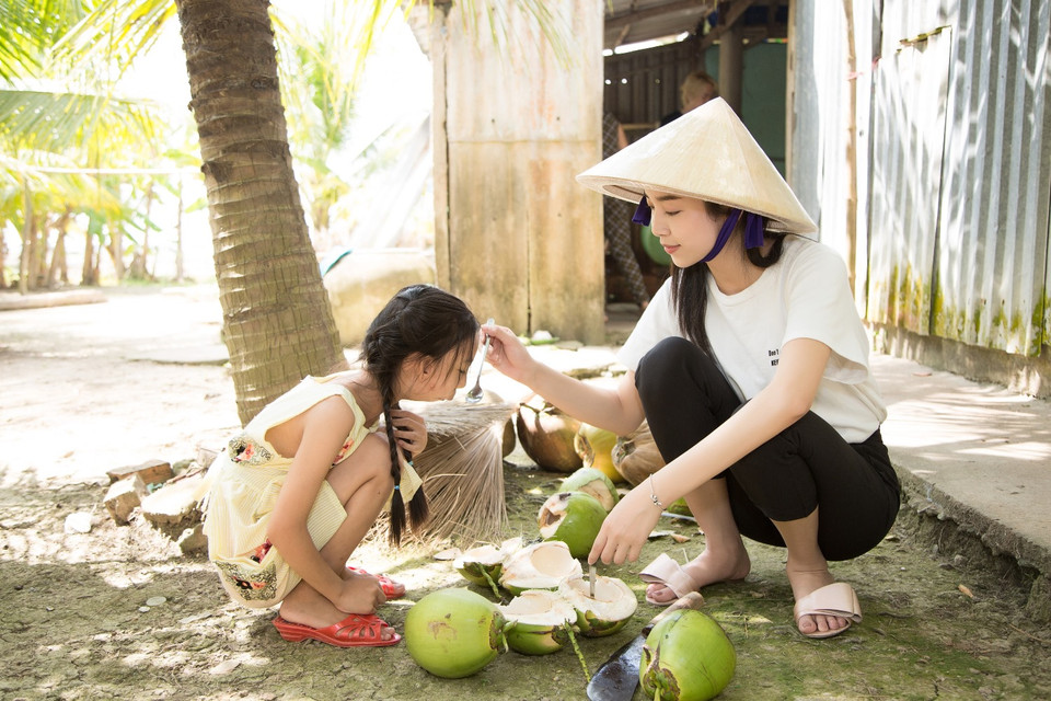 Hai chị em cùng thưởng thức nước dừa thơm ngon cây nhà lá vườn. (Ảnh: Tân Lê/Vietnam+) 