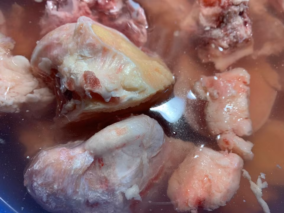 Nguyên liệu để làm món phở bò hương vị Hà Nội: 1kg xương ống bò, 500gr bắp bò hoa để làm bò tái (hoặc thêm gù bò để làm món bò chín), 1 củ gừng to, 2 bông đại hồi, 2 thảo quả, 1 nhánh nhỏ quế, 1gr hạt mùi già, 1gr tiểu hồi, 5 nụ đinh hương, 10gr tiêu sọ, 20gr sá sùng (nếu có nước phở có vị ngọt thơm tự nhiên), húng quế, hành tươi, hành tây 2 củ; đường phèn, hạt nêm, gia vị, muối, giấm, bánh phở. Sơ chế: Xương bò mua về ngâm trong nước muối và giấm khoảng 2 tiếng cho sạch mùi tanh hôi.(Ảnh: Mai Mai/Vietnam+)