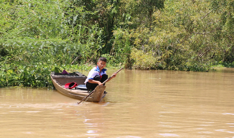 Nhiều em nhà nằm sâu trong khu dân cư, xuồng không thể vào được, các em phải bơi thuyền một đoạn để vào nhà. (Ảnh: Công Mạo/TTXVN)