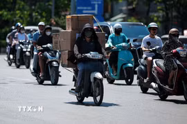 Người giao hàng bằng xe máy phải phủ kín người bằng áo chống nắng, khẩu trang và mũ để thích nghi với thời tiết khắc nghiệt. (Ảnh: Phạm Tuấn Anh/TTXVN)