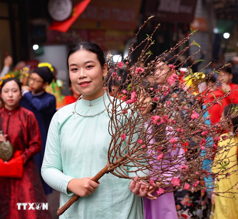 Thiếu nữ bên cành đào Xuân trong đoàn rước lễ cửa đình.(Ảnh: Thanh Tùng/TTXVN)