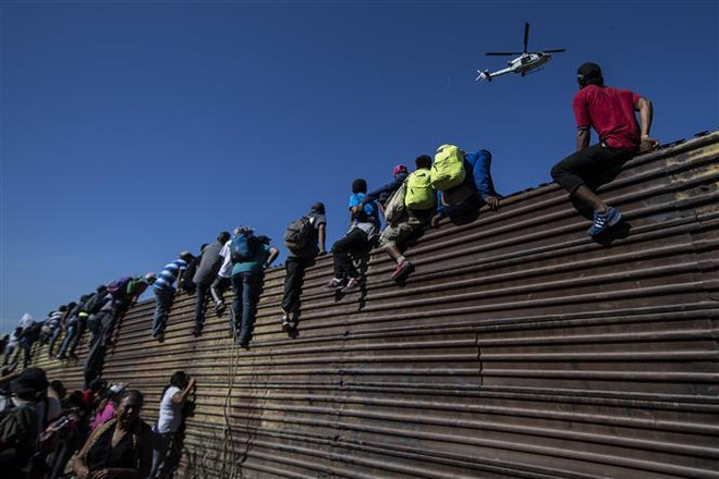 Người di cư vượt qua bức tường biên giới Mỹ-Mexico ở gần cửa khẩu El Chaparral, Tijuana, bang Baja California, Mexico. (Ảnh: AFP/TTXVN) Tổng thống Mexico kêu gọi đối thoại với Mỹ về vấn đề người di cư ảnh 1