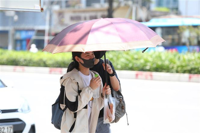 Người dân ra đường ngoài đeo khẩu trang còn che ô để tránh nắng và tia UV gây hại. (Ảnh: Thành Đạt/TTXVN) Trong 10 ngày tới, cả nước ngày nắng nóng, đêm có mưa và dông ảnh 2