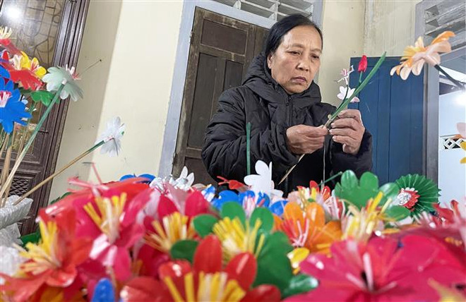 Các công đoạn để làm nên hoa giấy Thanh Tiên khá công phu và cầu kỳ. Sau khi cắt, dán tạo nên những loài hoa đẹp, nghệ nhân sẽ đính kết các loài hoa này tạo thành những cành hoa đầy màu sắc. (Ảnh: Mai Trang/TTXVN) Làng nghề truyền thống gìn giữ hồn Tết cổ truyền dân tộc ảnh 2