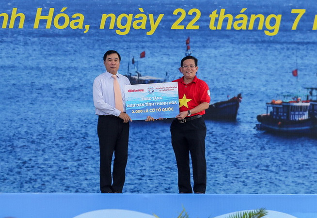 Ông Phạm Đăng Quyền, Phó chủ tịch UBND tỉnh Thanh Hóa (bên trái) đại diện địa phương nhận bảng tượng trưng 2.000 lá cờ từ tay Tổng biên tập Báo Người Lao Động Tô Đình Tuân. (Nguồn: nld.com.vn) Trao tặng 2.000 lá cờ Tổ quốc cho ngư dân tỉnh Thanh Hóa ảnh 1
