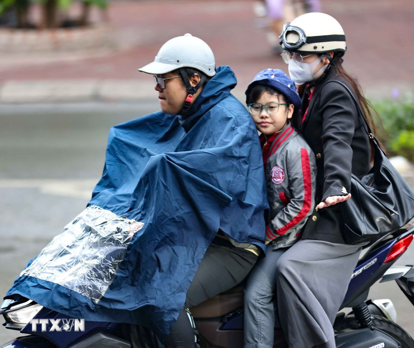 Một gia đình ra đường trong chiếc áo mưa khi trời có mưa phùn. (Ảnh: Thanh Tùng/TTXVN)