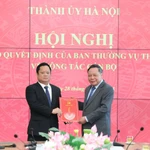 Phó Bí thư Thường trực Thành ủy Hà Nội Nguyễn Văn Phong trao quyết định của Ban Thường vụ Thành ủy Hà Nội và tặng hoa chúc mừng ông Vũ Minh Tuấn. (Ảnh: Quang Thái)