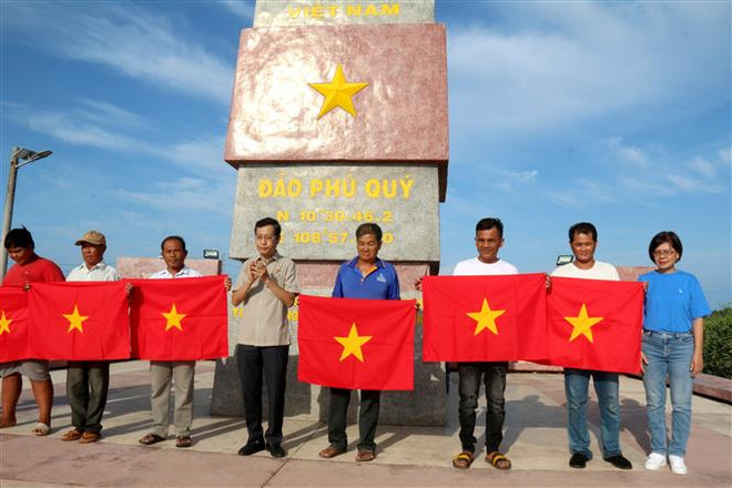 Đại diện lãnh đạo Cơ quan TTXVN khu vực phía Nam và lãnh đạo Công ty trách nhiệm hữu hạn một thành viên ITAXA tặng cờ Tổ quốc cho ngư dân tại Phú Quý. (Ảnh: Nguyễn Thanh/TTXVN) Tuổi trẻ Thông tấn xã Việt Nam hướng về biển, đảo quê hương ảnh 1