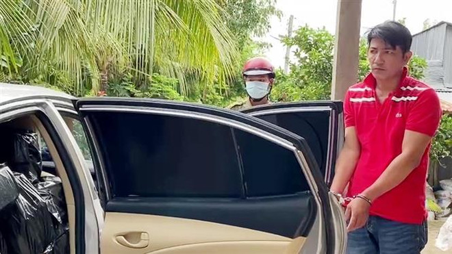 Đối tượng Nguyễn Văn Thắng (áo đỏ) cùng phương tiện bị lực lượng chức năng tạm giữ. (Ảnh: Công Mạo/TTXVN) An Giang: Bắt giữ xe ôtô vận chuyển gần 8.000 bao thuốc lá nhập lậu ảnh 1