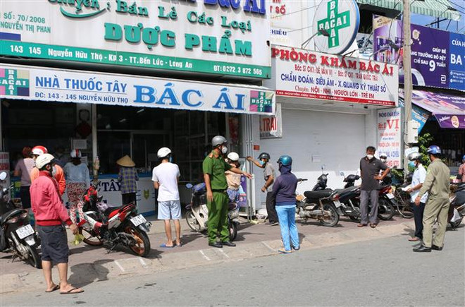 Lực lượng công an nhắc nhở người dân giữ khoảng cách an toàn khi mua hàng hóa, tại thị trấn Bến Lức, huyện Bến Lức, tỉnh Long An. (Ảnh: Thanh Bình/TTXVN) Ngày đầu nới lỏng giãn cách ở Long An: Có nơi chen lấn mua hàng hóa ảnh 1