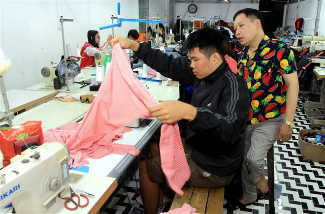 Mặc dù bị khuyết tật bẩm sinh nhưng bằng nghị lực và ý chí vươn lên, ông Phạm Văn Đáp (phải), Giám đốc Công ty trách nhiệm hữu hạn sản xuất và dịch vụ may mặc người khuyết tật ở xã Vũ Lễ, huyện Kiến Xương, tỉnh Thái Bình đã vượt qua khó khăn, vươn lên làm giàu và tạo việc làm cho những người cùng cảnh ngộ. (Ảnh: Thế Duyệt/TTXVN) Hỗ trợ người khuyết tật: Không chỉ cho 'con cá' mà cần 'chiếc cần câu' ảnh 3