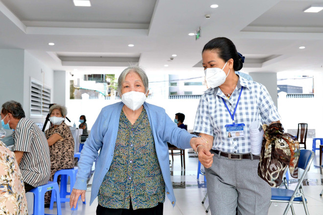 Các y bác sỹ Trung tâm Y tế quận 3, Thành phố Hồ Chí Minh, hỗ trợ, hướng dẫn người trên 65 tuổi, người mắc bệnh mãn tính, người thuộc hộ nghèo tiêm vaccine Moderna phòng COVID-19 đợt 5. (Ảnh: Thanh Vũ/TTXVN) Tiêm vaccine cho người nghèo: Niềm vui giữa bộn bề khó khăn ảnh 1