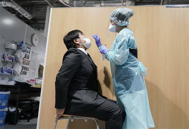 Nhân viên y tế lấy mẫu xét nghiệm COVID-19 tại Narita, Nhật Bản. (Ảnh: AFP/TTXVN) Nhật Bản cho phép bán lẻ kit xét nghiệm đồng thời cúm mùa và COVID-19 ảnh 1