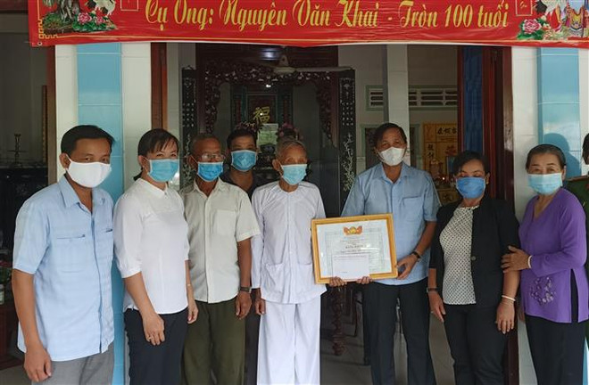 Cụ ông Nguyễn Văn Khai (thứ 5 từ trái sang), 100 tuổi đóng góp tiền tiết kiệm cho Quỹ phòng, chống dịch bệnh COVID-19 và được lãnh đạo Ủy ban MTTQ Việt Nam tỉnh Đồng Tháp đến trao Bằng khen 'Về hành động nhân ái ủng hộ phòng, chống dịch bệnh COVID-19.' (Ảnh: TTXVN phát) Cụ ông 100 tuổi dành tiền mừng thọ ủng hộ công tác phòng, chống dịch ảnh 1