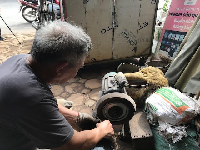 Người thợ rèn Đa Sỹ mài những lưỡi dao qua máy để làm sáng và loại bỏ những mạt sắt bám vào dao trong quá trình nung. (Nguồn: Vietnam+) Làng nghề 'đệ nhất dao kéo đất Thăng Long' và hành trình giữ lửa rèn ảnh 3