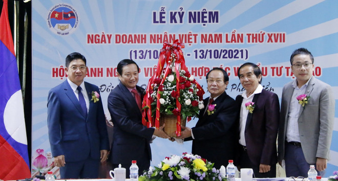 Đại sứ Nguyễn Bá Hùng đang trao lẵng hoa chúc mừng 17 năm ngày Doanh nhân Việt Nam cho ông Dương Đình Bảng, Chủ tịch lâm thời Hội doanh nghiệp Việt Nam hợp tác và đầu tư tại Lào. (Ảnh: Phạm Kiên/Vietnam+) Doanh nghiệp Việt có nhiều đóng góp cho phát triển kinh tế-xã hội Lào ảnh 1