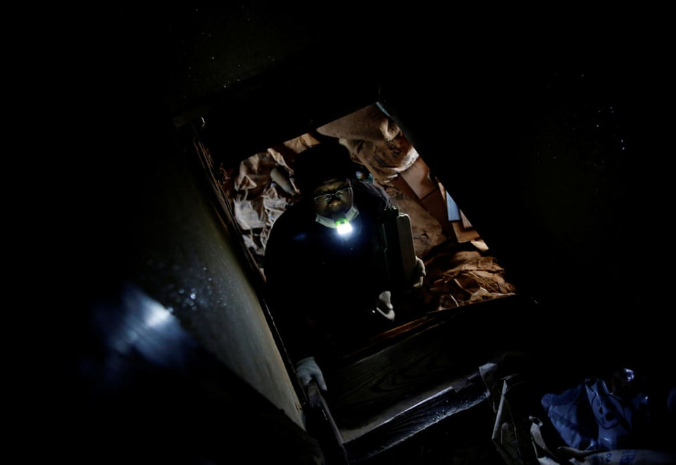 Sakae Kato ngậm đèn pin trong miệng khi trèo thang lên tầng hai một ngôi nhà bỏ hoang mà anh đã cải tạo thành nơi trú ẩn cho mèo. (Ảnh: Reuters)