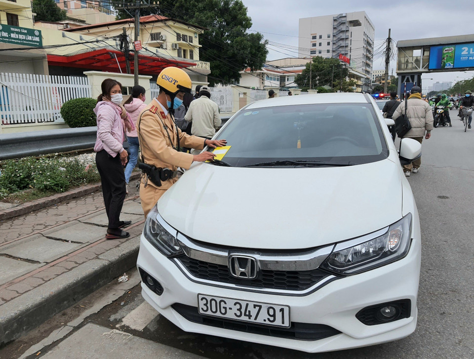 Cảnh sát giao thông dán phạt nguội đối với phương tiện dừng, đỗ trái phép trên đường Giải Phóng. (Ảnh: Doãn Tấn/TTXVN)