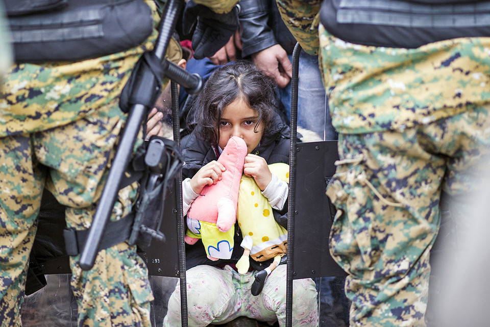Bé gái nhập cư ngồi trên đường ray giữa đám đông cảnh sát chống bạo động. (Ảnh: AFP)