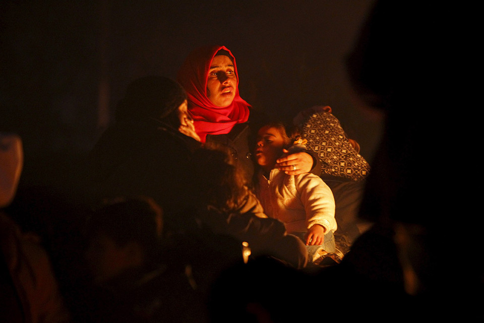 Người mẹ ủ ấm cho con cạnh đống lửa chờ được đăng ký nhập cư. (Ảnh: Reuters)