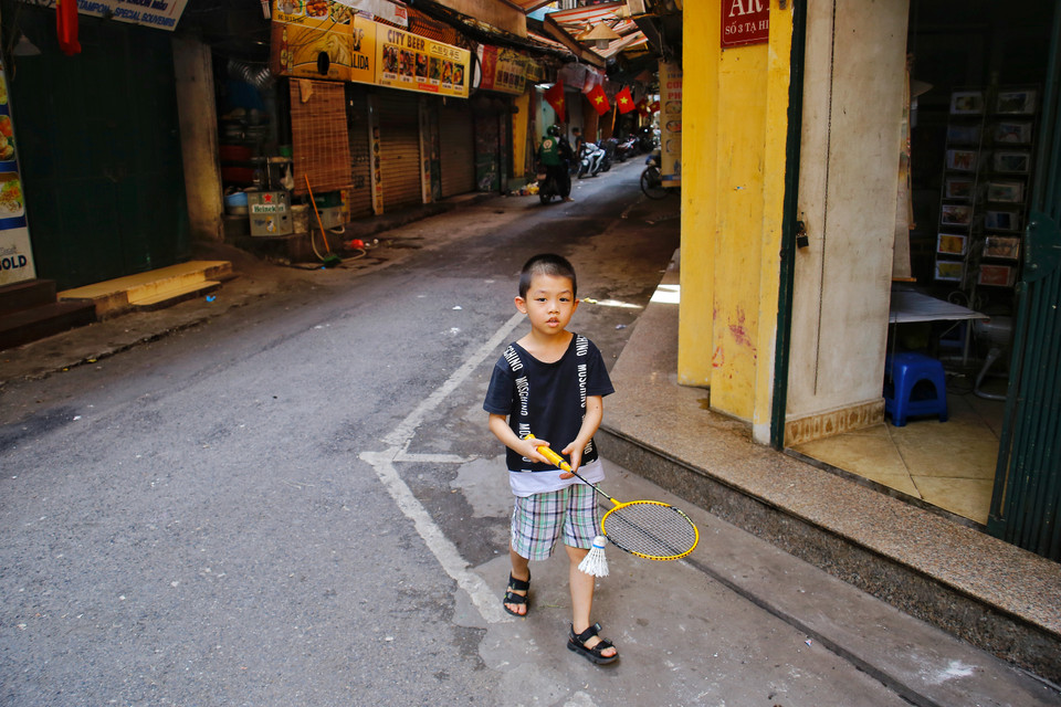  Em Tuấn Hải (lớp 1, trường tiểu học Trần Nhật Duật) hào hứng cho hay: “Cứ chiều đến là em mang vợt ra đây để đánh cầu lông, chỗ này rộng và vắng lắm ạ. Bình thường ở đây có đông người lắm nhưng bây giờ họ đóng cửa rồi. Nhà em thì bán bánh mỳ và chỉ có bán mang về thôi”. (Ảnh: Thế Mạnh/Vietnam+)