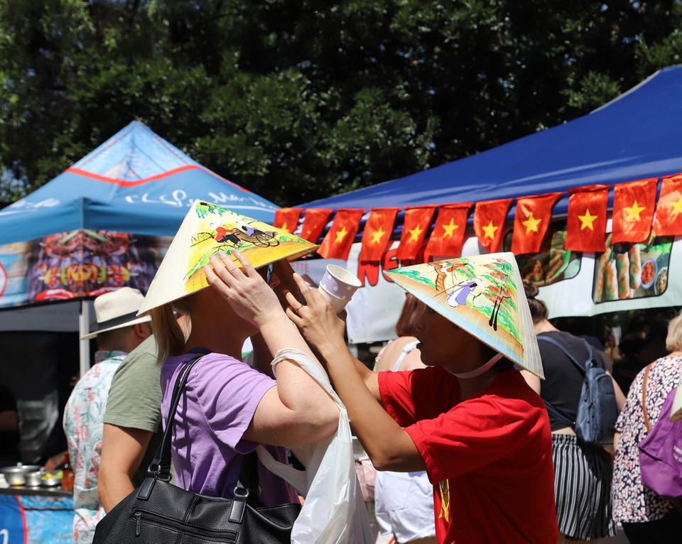 Một thành viên Ban tổ chức giúp đỡ một người khách Nam Phi đội nón lá Việt Nam tại sự kiện Ngày Phở Việt Nam tại Nam Phi 2023. (Ảnh: Hồng Minh/TTXVN)