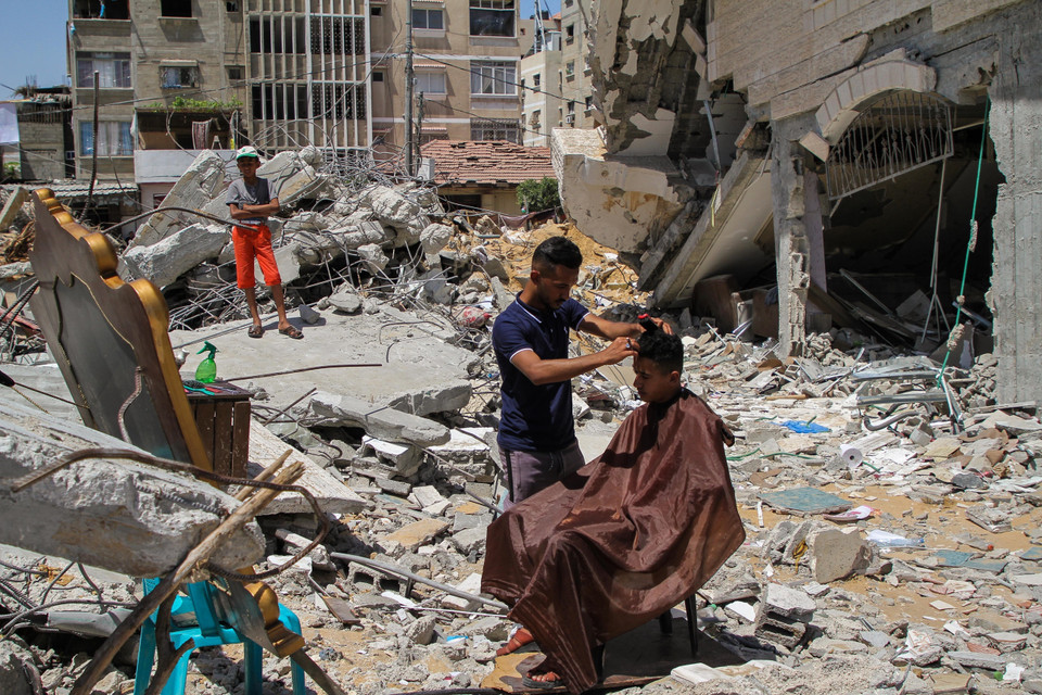 Người thợ cắt tóc Palestine cắt tóc miễn phí cho khách hàng bên căn nhà bị phá hủy sau cuộc không kích của Israel xuống thị trấn Beit Lahia, Dải Gaza, ngày 26/5/2021. (Ảnh: THX/TTXVN)