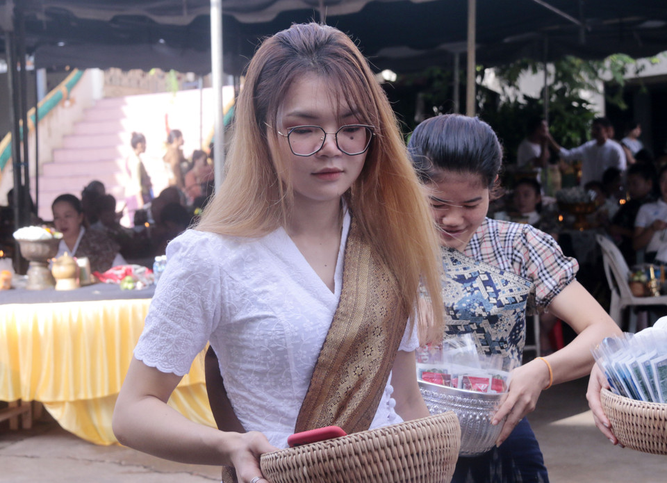 Hiện đại nhưng vẫn giữ được nét truyền thống, một thiếu nữ Lào đang chuẩn bị mua đồ để tham gia nghi thức Tak Bath để dâng lễ cho các nhà sư và những người đã khuất. (Ảnh: Phạm Kiên/Vietnam+)