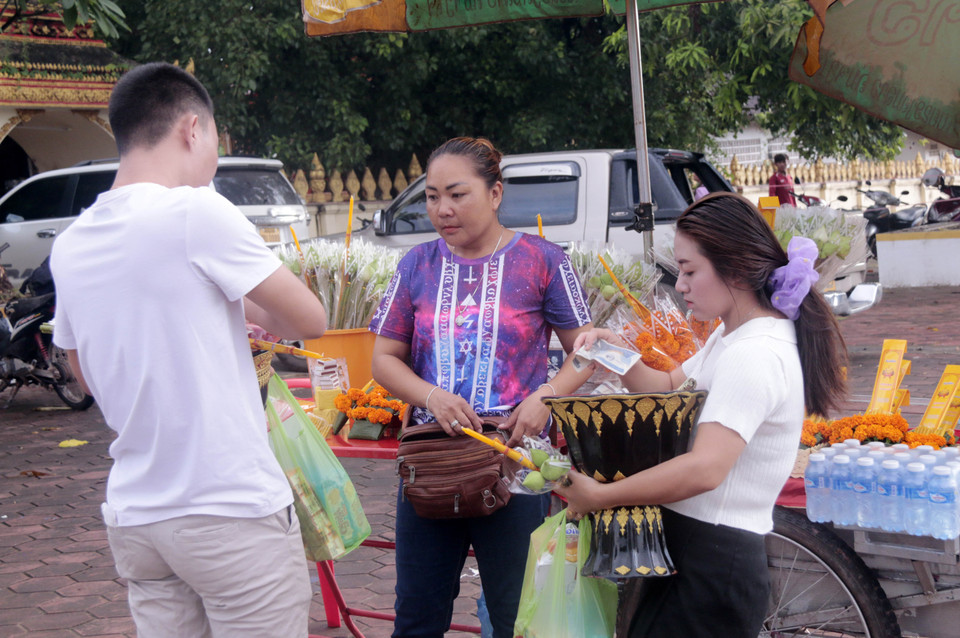 Cặp đôi nam nữ đang mua đồ lễ ngay trước cổng chùa That Luang Tay ở thủ đô Vientiane. (Ảnh: Phạm Kiên/Vietnam+)