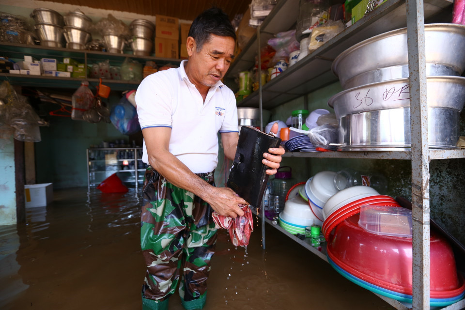 Nước đang rút dần, ông Nguyễn Quốc Thu, bán hàng tại khu chợ Vực tìm được cuốn sổ ghi đơn hàng bị chìm trong nước đã mấy ngày nay. (Ảnh: Minh Quyết/TTXVN)