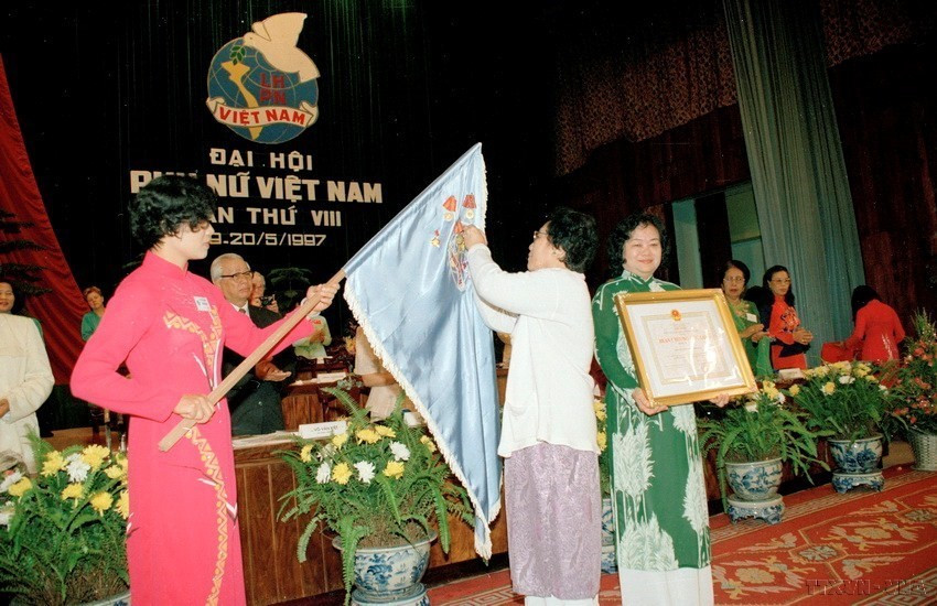 Phó Chủ tịch nước Nguyễn Thị Bình thay mặt Chủ tịch nước gắn Huân chương Độc lập hạng 3 lên lá cờ truyền thống của Hội Liên hiệp Phụ nữ Việt Nam tại Đại hội đại biểu Phụ nữ toàn quốc lần thứ VIII (5/1997). (Ảnh: TTXVN)