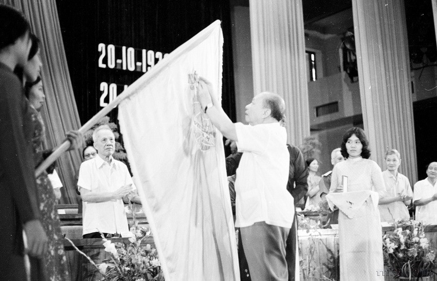 Chủ tịch Quốc hội Trường Chinh gắn Huân chương Hồ Chí Minh lên lá cờ truyền thống của Hội tại Lễ míttinh kỷ niệm 50 năm Ngày thành lập Hội Liên hiệp Phụ nữ Việt Nam (18/10/1980). (Ảnh: TTXVN)