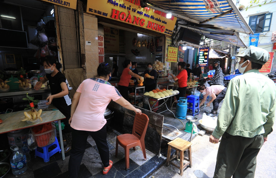 Lực lượng chức năng phường Hàng Bạc tuyên truyền, nhắc nhở người dân không họp chợ, tránh tụ tập đông người để phòng chống dịch. (Ảnh: Thành Đạt/TTXVN)