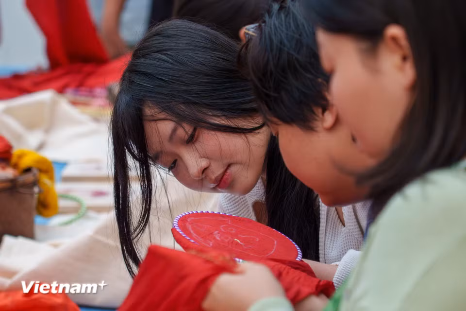 Các bạn trẻ chăm chút từng đường kim mũi chỉ trên nền lụa đỏ, cùng kết nối với di sản nghề dệt may thủ công truyền thống xứ Quảng. (Ảnh: Thanh Phong/Vietnam+)