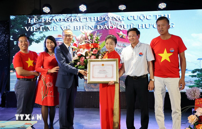 Đại sứ Vũ Quang Minh trao Giấy khen và tặng hoa cho bà Bùi Thị Thu Minh, Trưởng ban liên lạc người Việt tại châu Âu “Vì biển đảo Việt Nam,” Chủ tịch Câu lạc bộ Trường Sa tại Đức. (Ảnh: Thu Hằng/TTXVN) ttxvn-3006-cuoc-thi-bien-dao-kieu-bao-duc-2.jpg