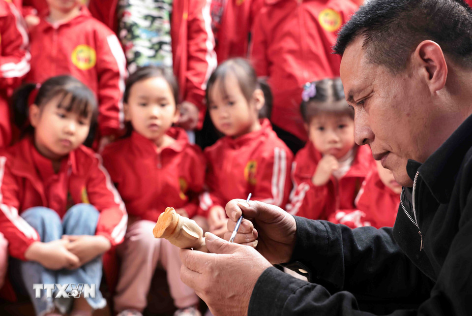 Nghệ nhân Nguyễn Văn Phi hướng dẫn cách sơn quân trò rối cho các "khách du lịch nhí." (Ảnh: Trần Việt/TTXVN)