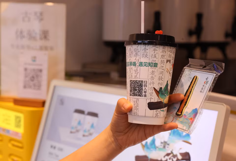Khách thăm quan mua trà, quét mã QR và thưởng thức trà trong âm thanh của cổ cầm, đồng thời không quên “check–in” với ly trà sữa và món quà lưu niệm mang hình dáng cổ cầm. (Ảnh: Văn Điệp/TTXVN)
