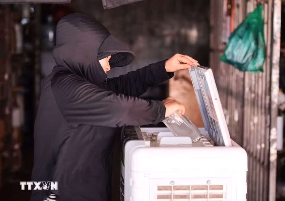 Một tiểu thương tại Chợ Long Biên cho thêm đá vào quạt hơi nước để làm dịu không khí, chống chọi với đợt nắng nóng gay gắt. (Ảnh: Hoàng Hiếu/TTXVN)