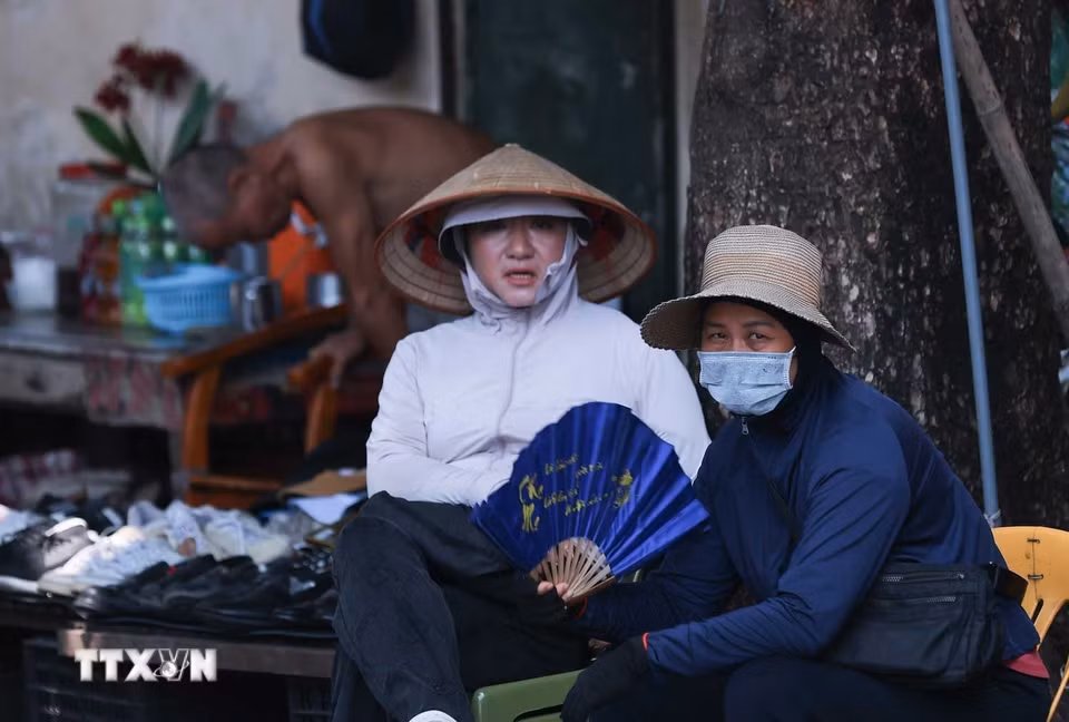 Dù ngồi trong bóng râm, quạt, khẩu trang, áo chống nắng vẫn luôn là trang bị không thể thiếu của các tiểu thương chợ Đồng Xuân trong những ngày Hà Nội "rực lửa" (Ảnh: Hoàng Hiếu/TTXVN)