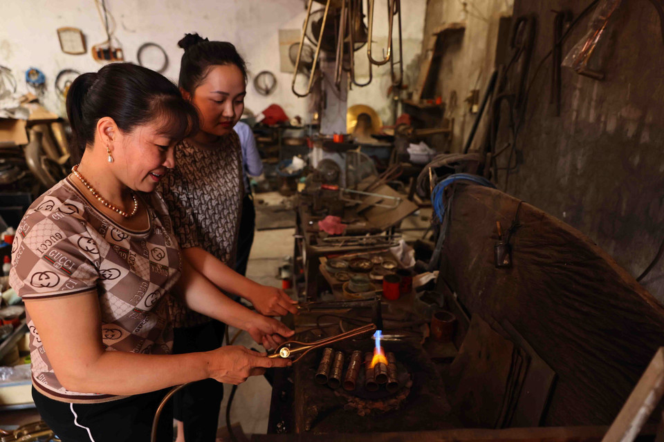 Vợ và con gái ông Nguyễn Văn Hưởng với công đoạn hàn pháo của kèn. (Ảnh: Minh Đức/TTXVN)