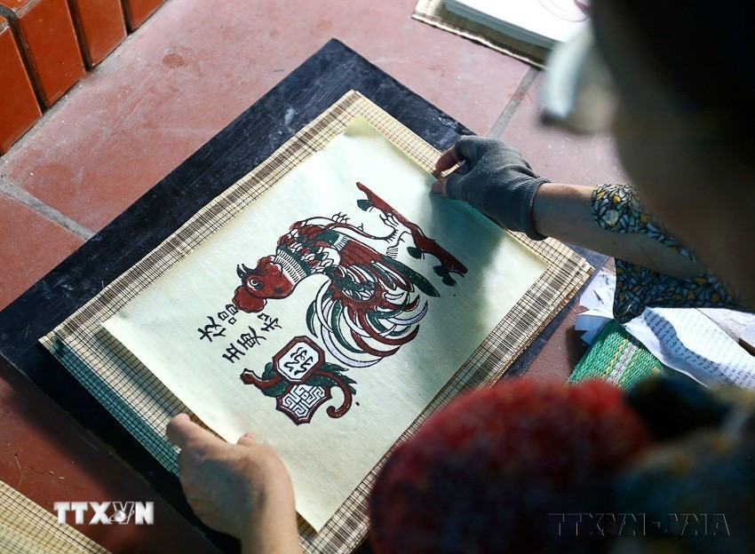 Tranh Đông Hồ sau khi in xong được gỡ ra khỏi ván in, dán lên khay tre rồi mang ra phơi ở những nơi thoáng mát. Tranh khô rồi mới tiếp tục lần lượt in các màu khác. Bản nét đen bao giờ cũng được in cuối cùng. (Ảnh: Minh Quyết/TTXVN)