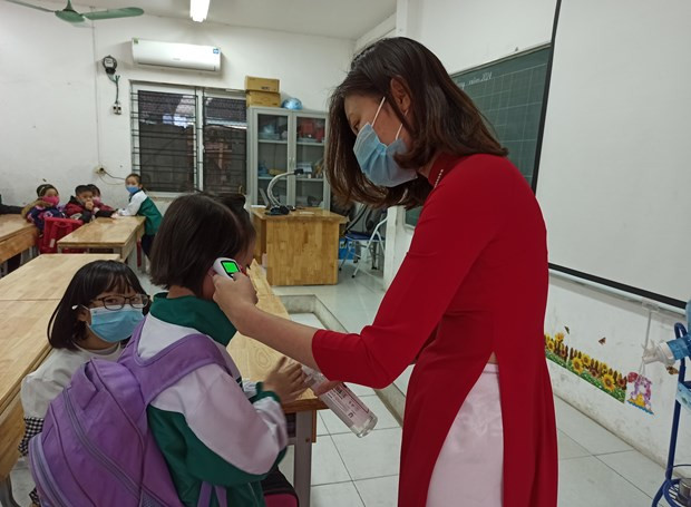 Giáo viên đo thân nhiệt cho học sinh trước khi vào lớp. (Ảnh: Phạm Mai/Vietnam+) Hà Nội: Các cơ sở giáo dục lên phương án sẵn sàng đón học sinh ảnh 2